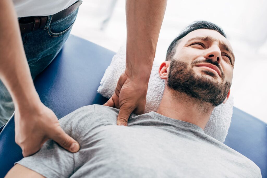 Coburn Chiropractic - chiropractor massaging shoulder of man lying on ma 6RB9W2K